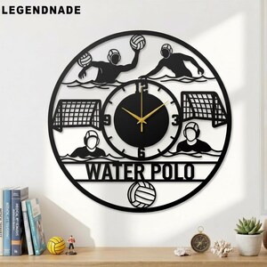 Könnte beinhalten: Schwarze Metall-Wanduhr mit Wasserball-Motiv. Die Uhr zeigt Silhouetten von Wasserballspielern, Toren und einem Ball. Die Worte "WATER POLO" sind unter dem Zifferblatt zu sehen. Die Zeiger der Uhr sind goldfarben.