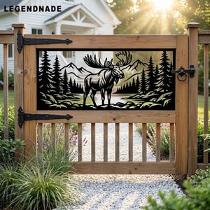 May include: A wooden gate featuring a black metal insert with a laser-cut design of a moose standing in a forest with mountains in the background. The gate includes black metal hinges and the text LEGENDNADE is visible in the top left corner.