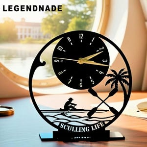 May include: Black decorative clock with a circular face and gold hands. The clock features a silhouette of a person rowing a boat, palm trees, and crossed oars. The text "SCULLING LIFE" is at the bottom. The brand name "LEGENDNADE" is at the top.