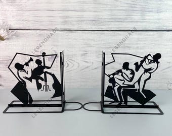 Puede incluir: Dos sujetalibros de metal negro con la silueta de músicos tocando instrumentos. Los sujetalibros están diseñados para sostener los libros en posición vertical en una estantería o un escritorio.