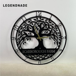 Könnte beinhalten: Schwarze Metall-Wanduhr mit einem Lebensbaum-Design. Die Uhr hat eine runde Form mit römischen Ziffern und goldfarbenen Zeigern. Der Text "SCARBOROUGH FARM" ist unten zu sehen. Der Markenname "LEGENDNADE" steht oben.