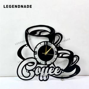 Op de afbeelding: Zwarte wandklok met een koffiethema. De klok heeft twee silhouetten van koffiekopjes, het woord "Coffee" en een ronde wijzerplaat met gouden wijzers. De tekst "LEGENDNADE" staat bovenaan.