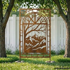 May include: A brown metal garden screen with a nature-inspired design. The screen depicts a tree, mountains, and a forest scene. It is set in a garden with grass, trees, and a white fence in the background. The screen is designed for outdoor use.
