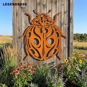 May include: A rust-colored metal wall art piece shaped like a beetle with intricate cut-out patterns. The insect silhouette features symmetrical curves and open spaces throughout its body, with the text LEGENDNADE visible in the top left corner.