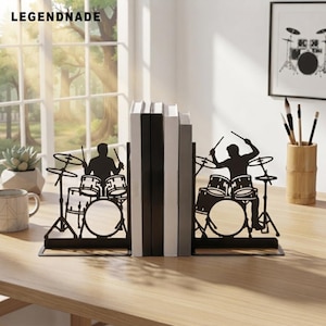 May include: A pair of black metal bookends featuring a silhouette design of a drummer playing a drum kit. The two pieces are positioned on either side of a row of books, each depicting a musician with drumsticks, cymbals, and drums.