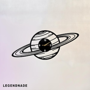 May include: Black and white wall clock in the shape of Saturn with a black clock face and gold hands. The clock has a unique design with the word LEGENDNADE at the bottom.