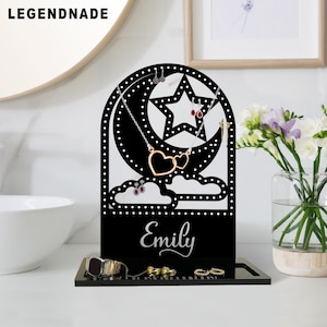 May include: Black jewelry display stand with a crescent moon and star design. The stand features a heart-shaped necklace, earrings, and a tray for rings and bracelets. The name "Emily" is written on the stand.