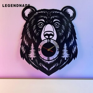 May include: Black bear head wall clock with a clock face at the center. The clock face has black numbers and hands with a gold center. The clock is made of a dark material and has the word LEGENDNADE at the top left.