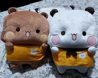 May include: Two plush toys, one brown with a yellow shirt and the other white with a yellow shirt. Both toys have cute cartoon faces with big eyes and smiling mouths.