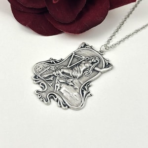 May include: Silver necklace with a pendant featuring a detailed, ornate design of a woman holding a scale. The pendant is attached to a silver chain.
