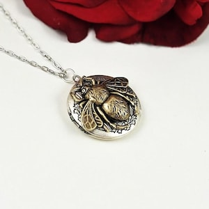 May include: A silver chain necklace with a locket pendant featuring a detailed bee design. The locket is made of silver and gold metal and has a textured finish.