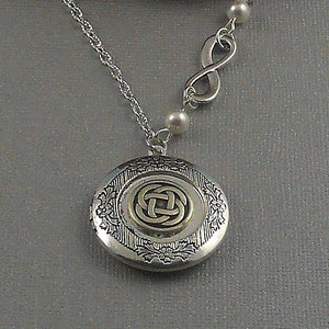 Op de afbeelding: Zilverkleurige ketting met een ronde medaillon met een Keltisch knoopontwerp. De medaillon is versierd met bloemendetails en hangt aan een fijne ketting. Een oneindigheidssymbool en kleine parels completeren het ontwerp.