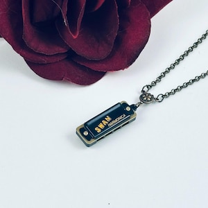 May include: A black harmonica necklace with a gold chain and a gold 'SWAN HARMONICA' inscription.