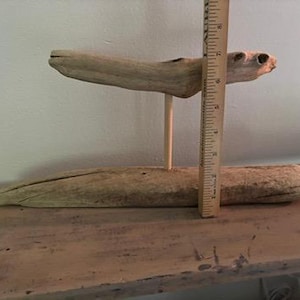 May include: A rustic, two-tiered wooden display stand made from driftwood. The top tier is supported by a single wooden dowel. A wooden ruler is placed next to the stand, showing its height.