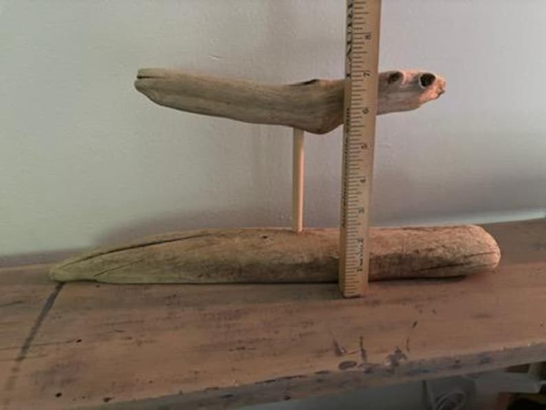 May include: A rustic, two-tiered wooden display stand made from driftwood. The top tier is supported by a single wooden dowel. A wooden ruler is placed next to the stand, showing its height.