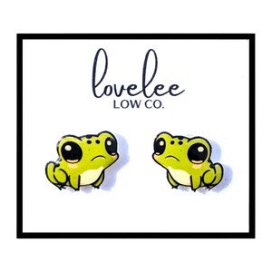 Könnte beinhalten: Ein Paar grüne Frosch-Ohrstecker mit schwarzen Augen. Die Ohrringe befinden sich auf einem weißen Hintergrund mit dem Text "lovelee LOW CO."