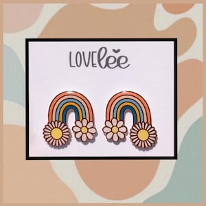 May include: A pair of rainbow-shaped earrings with daisy accents. The earrings feature a retro color palette of orange, yellow, blue, and cream. The word "LOVElee" is printed at the top of the card.