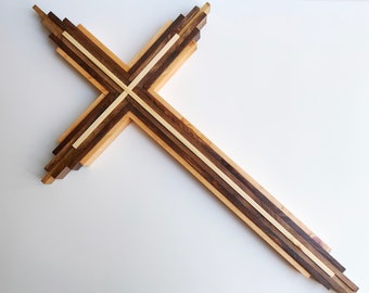 May include: A large wooden cross made of multiple strips of light and dark wood. The cross is arranged in a layered pattern, with the strips of wood overlapping each other.