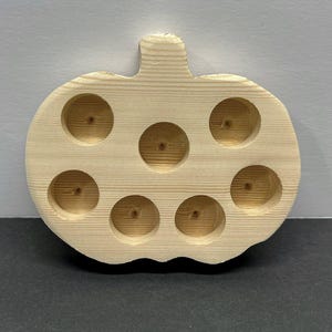 Op de afbeelding: Een houten pompoenvormige dienblad met zeven cirkelvormige inkepingen. De dienblad is gemaakt van lichtgekleurd hout en heeft een steel aan de bovenkant. De inkepingen zijn ontworpen om kleine items in te plaatsen.