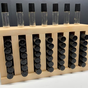 May include: A wooden storage rack with 7 rows of 6 slots, each slot holding a black and clear glass roller bottle. The rack is made of light wood and has a natural finish.