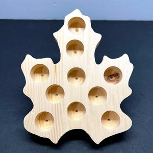 Op de afbeelding: Een houten blad-vormige dienblad met elf cirkelvormige inkepingen. De dienblad is gemaakt van lichtgekleurd hout en heeft een natuurlijke afwerking. Het ontwerp doet denken aan een esdoornblad, ideaal voor kleine items.