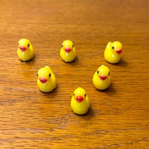 May include: Six yellow rubber duck figurines with red beaks and black eyes arranged in a semi-circle on a wooden surface.