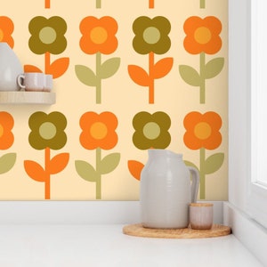 May include: A kitchen wall with a retro wallpaper pattern featuring orange and green flowers. The wallpaper has a cream background. A white pitcher and a small white jar are on a wooden coaster on a white countertop.