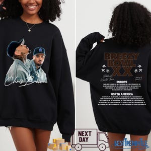 May include: Black sweatshirt featuring a Chris Brown image on the front and a tour graphic on the back. The front displays a photo of Chris Brown with his signature. The back lists tour dates for Europe and North America.