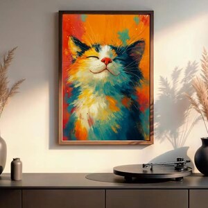 May include: A framed art print of a smiling cat with closed eyes. The cat's fur is a mix of white, blue, orange, and yellow. The background is a blend of orange and red. The artwork is displayed above a dark gray cabinet.