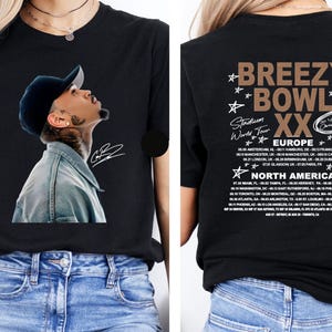 May include: Black t-shirt featuring a portrait of a man wearing a cap and denim jacket. The front of the shirt has a signature. The back of the shirt has the text "BREEZY BOWL XX Stadium World Tour" and a list of tour dates.