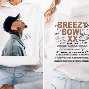 May include: White hoodie featuring a portrait of a man wearing a black cap and denim jacket, with his signature. The back of the hoodie displays "Breezy Bowl XX" tour dates for Europe and North America.