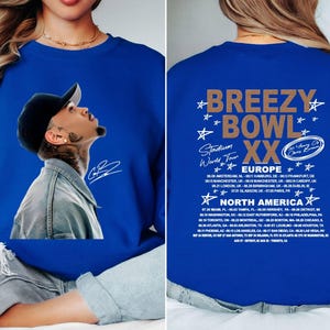 May include: Royal blue sweatshirt featuring a portrait of a man wearing a black cap, with a signature. The back of the sweatshirt displays the text "Breezy Bowl XX Stadium World Tour" with a list of European and North American tour dates.
