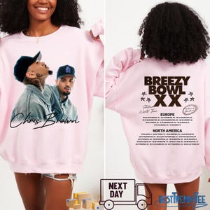 May include: A light pink sweatshirt featuring a graphic of Chris Brown on the front. The back of the sweatshirt displays "Breezy Bowl XX World Tour" text and a list of tour dates in Europe and North America.