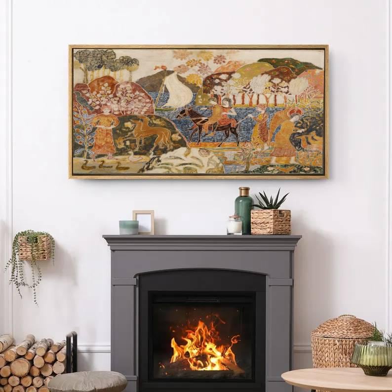 May include: A framed artwork with a gold-colored frame depicts a colorful, detailed scene with figures, animals, and trees. The artwork is mounted above a gray fireplace with a burning fire inside.