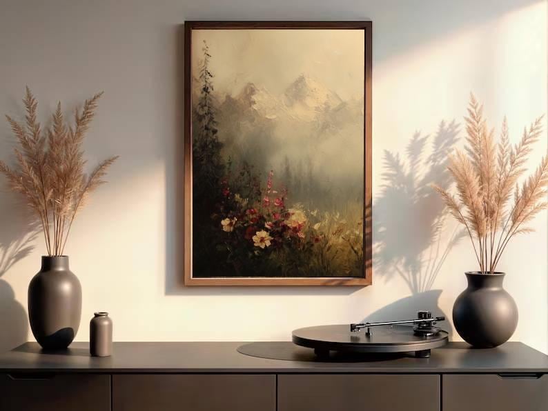 May include: A framed landscape painting depicts a mountain scene with flowers. Two dark vases with dried plants flank the painting. A record player sits on a dark cabinet, creating a serene, artistic display.