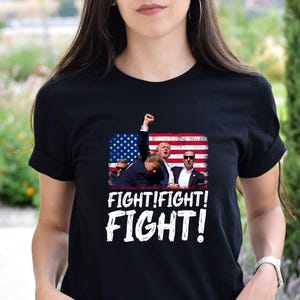 May include: Black t-shirt with a graphic of a group of people in front of an American flag. The text "Fight! Fight! Fight!" is printed below the graphic.
