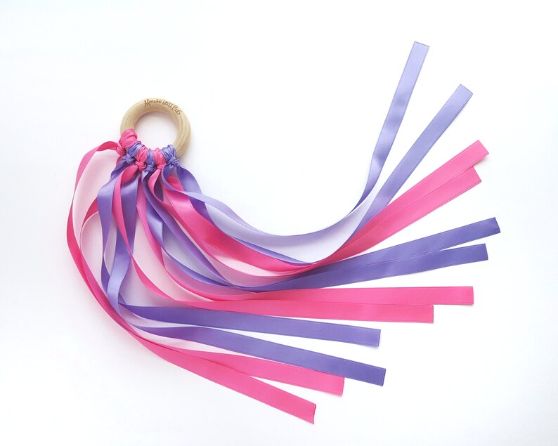 Op de afbeelding: Een houten ring met een geknoopte lintstreamer. De streamer is gemaakt van roze en paarse satijnen linten.