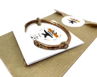Può includere: Un braccialetto in rame martellato con una finitura rustica. Il braccialetto è confezionato in una busta di carta marrone con un piccolo biglietto con un logo.