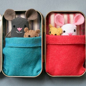 May include: Two small tin boxes with fabric lining. One box has a gray mouse with a pink nose and a brown bear inside. The other box has a white mouse with pink ears and a yellow bear inside. Both boxes have a red and white striped fabric lining.