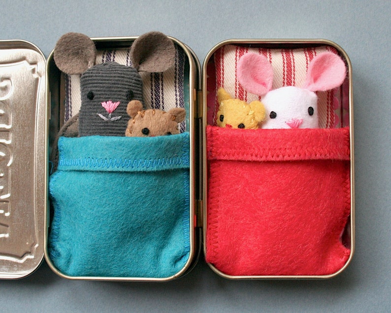 May include: Two small tin boxes with fabric lining. One box has a gray mouse with a pink nose and a brown bear inside. The other box has a white mouse with pink ears and a yellow bear inside. Both boxes have a red and white striped fabric lining.