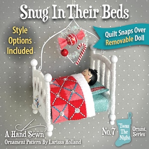 May include: A white miniature bed ornament featuring a doll with black hair tucked under a red and pink quilted blanket with blue stitching and sequins. Above the bed hangs a wire mobile with a red candy and a candy cane. Text reads Snug In Their Beds.