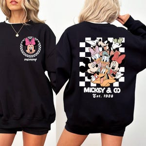 May include: Black sweatshirt with a checkered pattern on the back and a Mickey Mouse and friends graphic. The text "Mickey & Co. Est. 1928" is printed below the graphic. The front of the sweatshirt has a small graphic of Minnie Mouse with the word "mommy" printed below it.