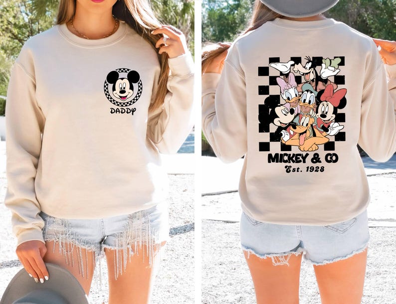 Puede incluir: Una sudadera beige con un patr&oacute;n de cuadros blanco y negro y un gr&aacute;fico de Mickey Mouse en la parte delantera. La parte posterior de la sudadera tiene un patr&oacute;n de cuadros blanco y negro con Mickey Mouse y sus amigos. El texto "Mickey & Co. Est. 1928" est&aacute; impreso en la parte posterior de la sudadera.