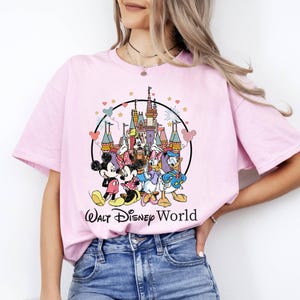 Puede incluir: Camiseta rosa con un gr&aacute;fico de Mickey Mouse, Minnie Mouse, Donald Duck, Goofy y Pluto frente al Castillo de Cenicienta. El gr&aacute;fico est&aacute; rodeado por un c&iacute;rculo con estrellas y corazones. El texto "Walt Disney World" est&aacute; impreso debajo del gr&aacute;fico.