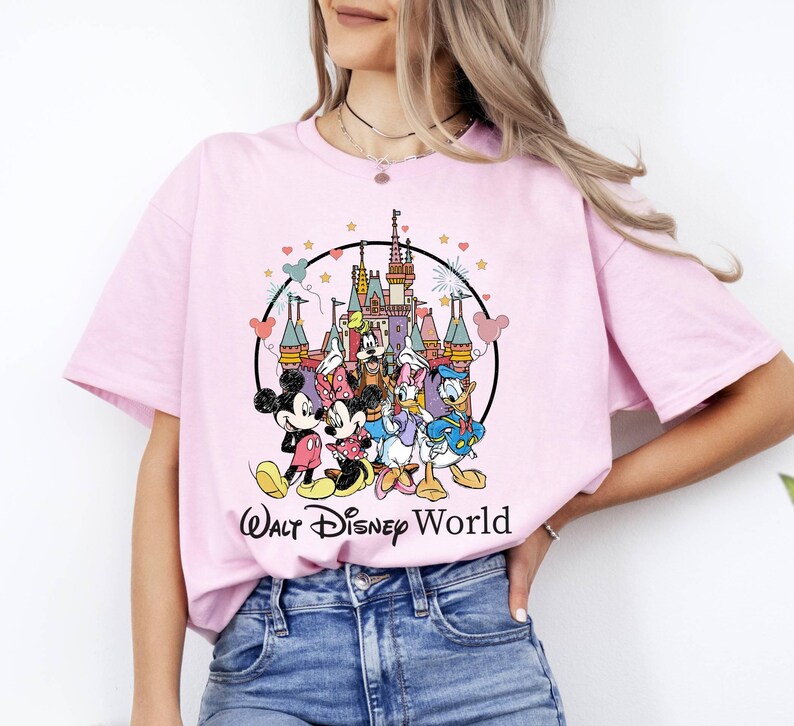 Puede incluir: Camiseta rosa con un gr&aacute;fico de Mickey Mouse, Minnie Mouse, Donald Duck, Goofy y Pluto frente al Castillo de Cenicienta. El gr&aacute;fico est&aacute; rodeado por un c&iacute;rculo con estrellas y corazones. El texto "Walt Disney World" est&aacute; impreso debajo del gr&aacute;fico.