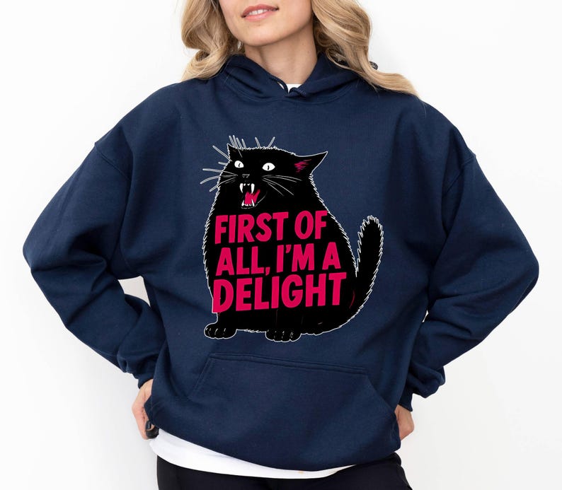 Op de afbeelding: Marineblauwe hoodie met een zwarte kattenafbeelding en de roze tekst "FIRST OF ALL, I'M A DELIGHT". De kat heeft een open mond. De sweatshirt heeft een voorzak en een capuchon met trekkoord. Een casual, comfortabel kledingstuk.