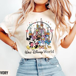 Puede incluir: Una camiseta blanca con una ilustraci&oacute;n de estilo vintage de Mickey Mouse, Minnie Mouse, Donald Duck, Goofy y Pluto frente al Castillo de Cenicienta. El texto "Walt Disney World" est&aacute; impreso debajo de la ilustraci&oacute;n.
