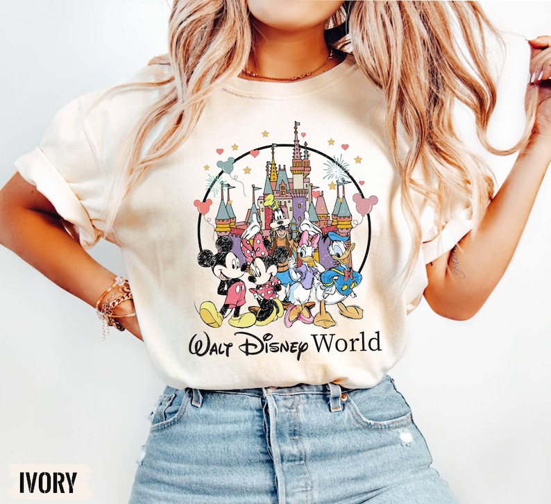 Puede incluir: Una camiseta blanca con una ilustraci&oacute;n de estilo vintage de Mickey Mouse, Minnie Mouse, Donald Duck, Goofy y Pluto frente al Castillo de Cenicienta. El texto "Walt Disney World" est&aacute; impreso debajo de la ilustraci&oacute;n.