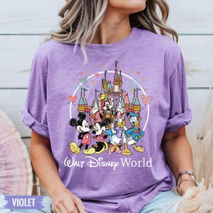 Puede incluir: Una camiseta morada con un gr&aacute;fico de Mickey Mouse, Minnie Mouse, Donald Duck, Goofy y Pluto frente al Castillo de Cenicienta. El texto "Walt Disney World" est&aacute; impreso debajo del gr&aacute;fico.