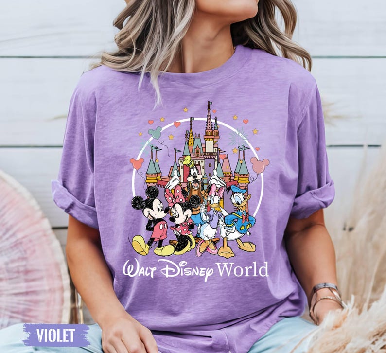 Puede incluir: Una camiseta morada con un gr&aacute;fico de Mickey Mouse, Minnie Mouse, Donald Duck, Goofy y Pluto frente al Castillo de Cenicienta. El texto "Walt Disney World" est&aacute; impreso debajo del gr&aacute;fico.
